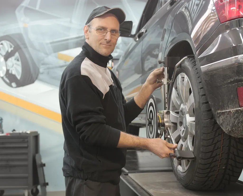 Technician adjusting wheel-alignment equipment attached to a car wheel