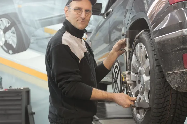 Technician adjusting wheel-alignment equipment attached to a car wheel